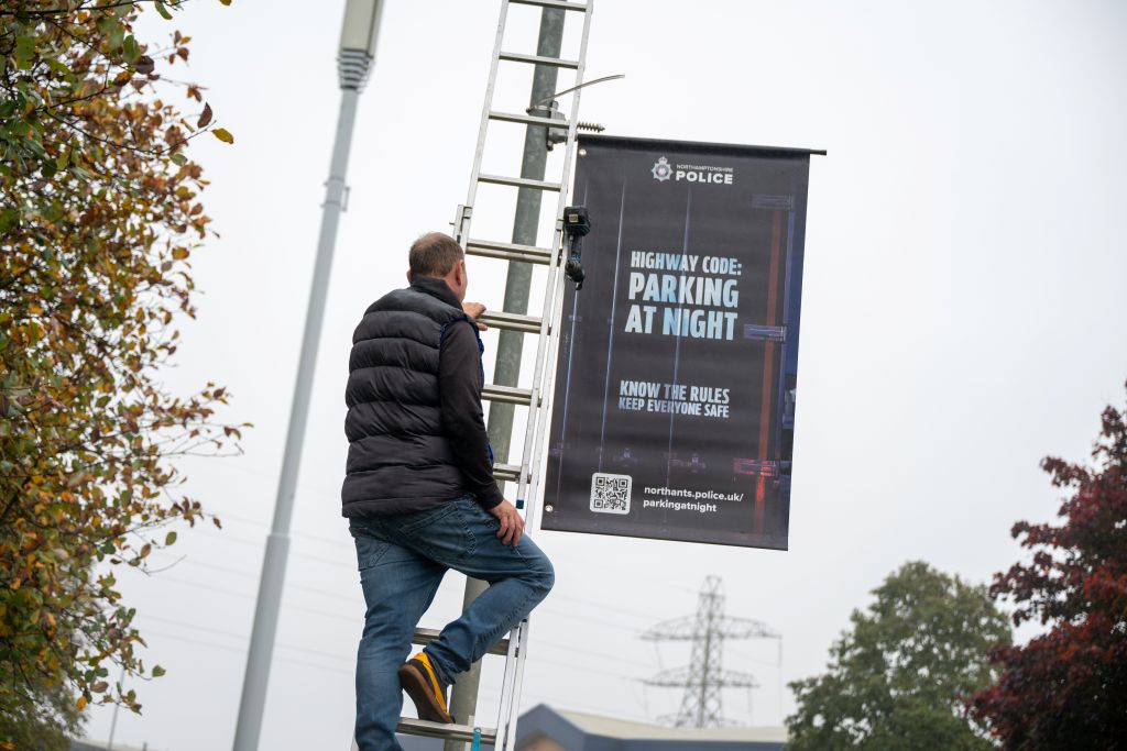 Informational parking banner being hung off a lamppost. There is a man up a ladder installing it.