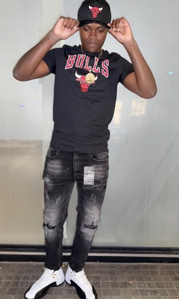 A young man in a black Chicago Bulls t-shirt and cap posing against a plain wall.